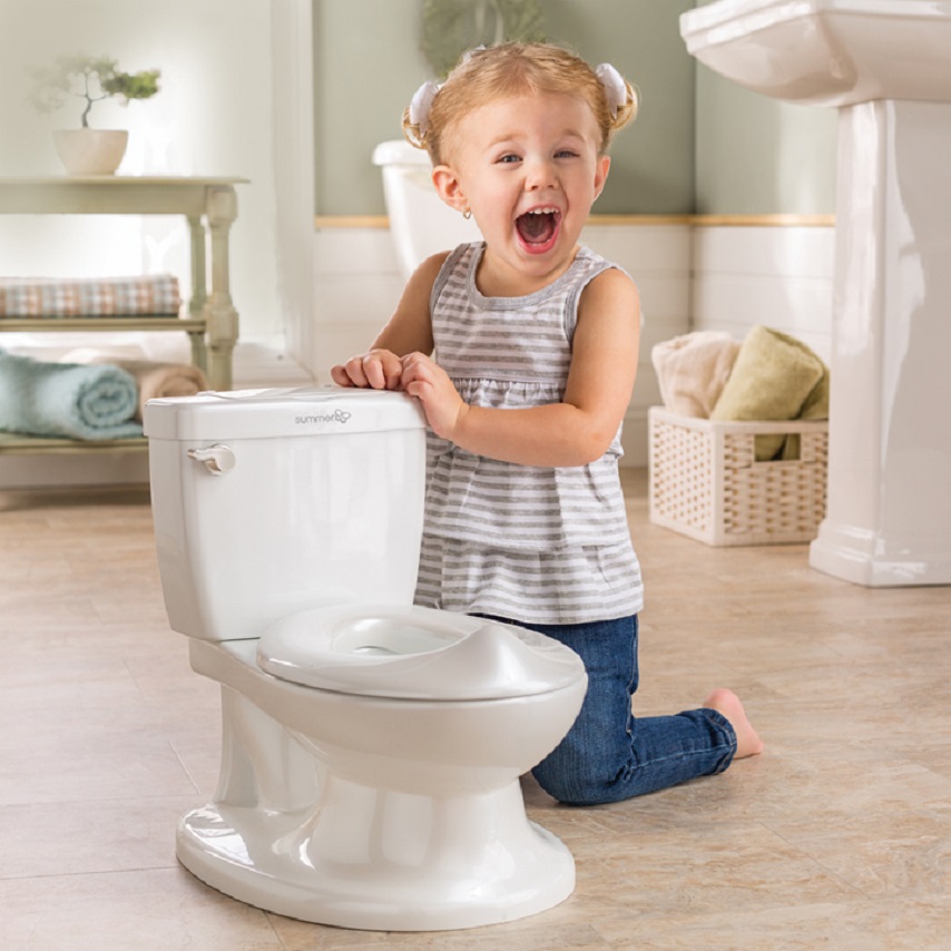 picture of a baby girl beside a potty in a shape of a toilet in the bathroom